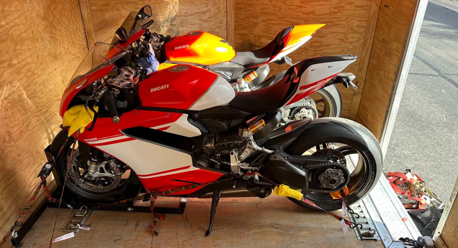 Two Ducati sport bikes strapped upright in wheel chocks inside a plywood-lined enclosed trailer.