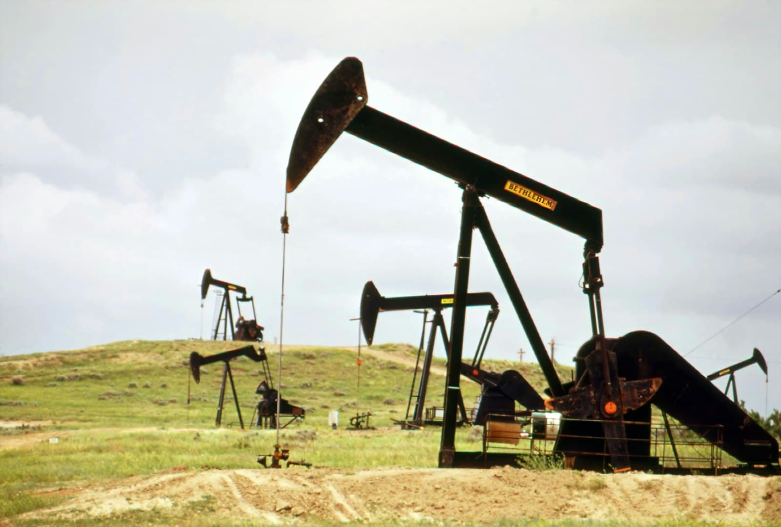 A row of pumpjacks across an oil field under a hazy sky.