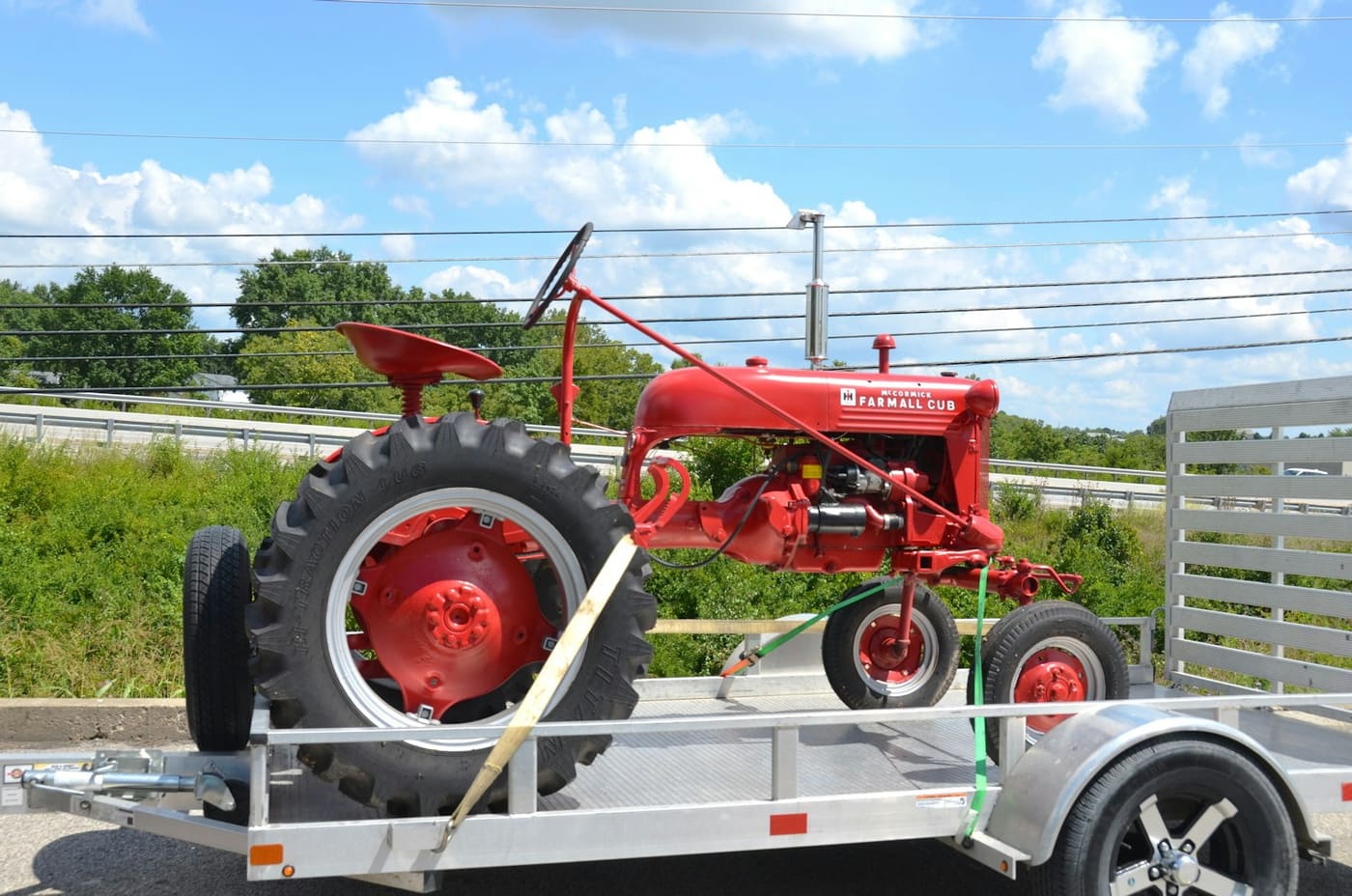 A red vintage tractor strapped down on an open flatbed trailer.